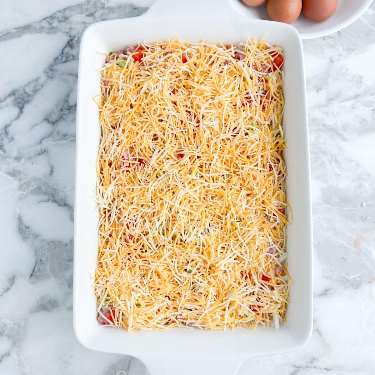 Casserole dish filled with shredded cheese and diced vegetables.