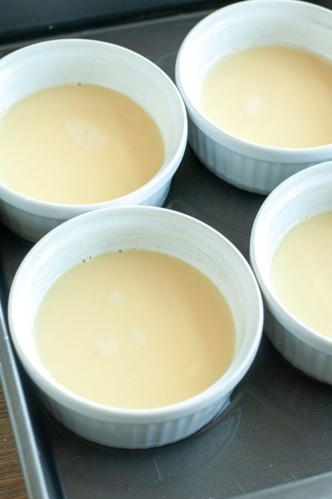 4 ramekins with egg custard in a baking dish with water