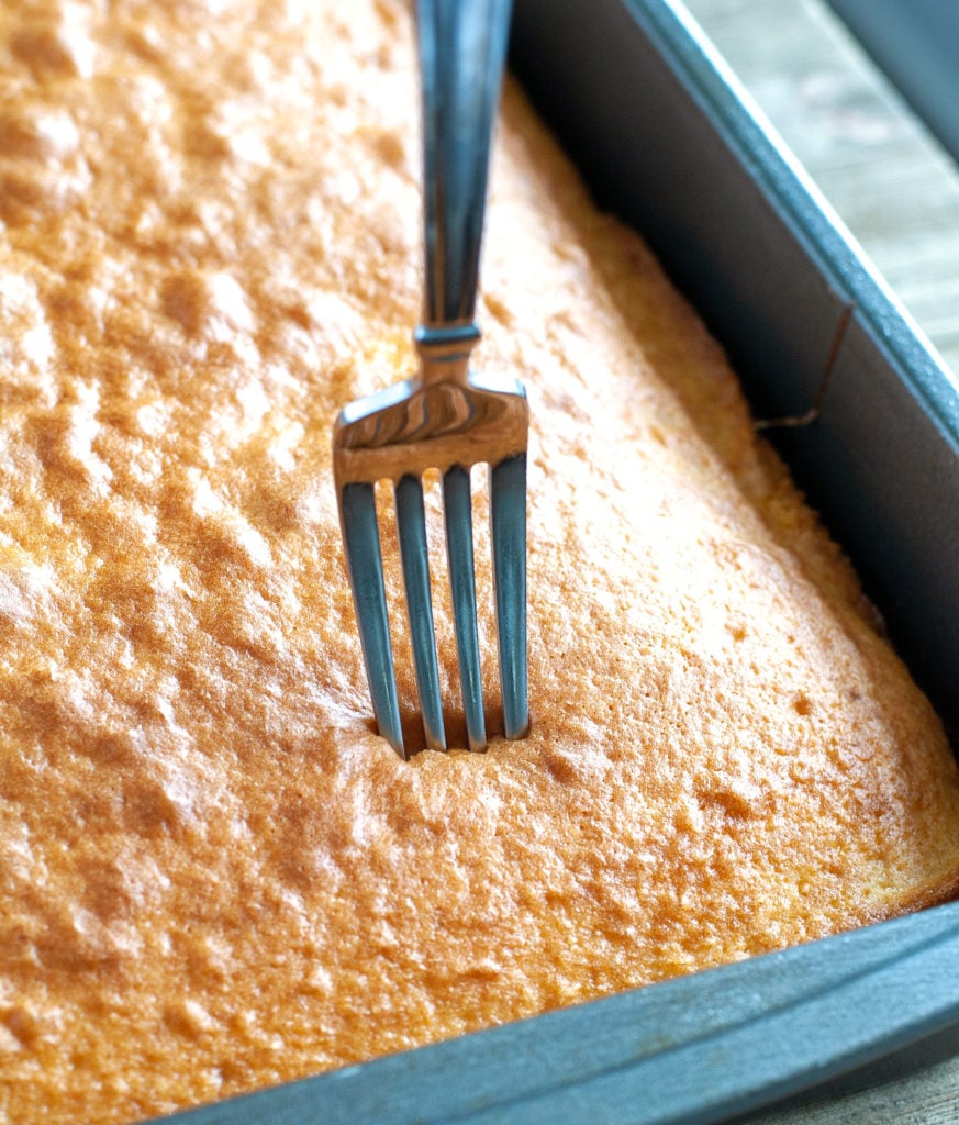 Baked yellow cake in a pan with a fork poking holes into the cake