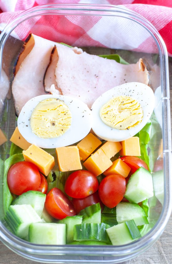 Meal prep container filled with turkey, hard boiled egg, cheese, tomato and cucumber