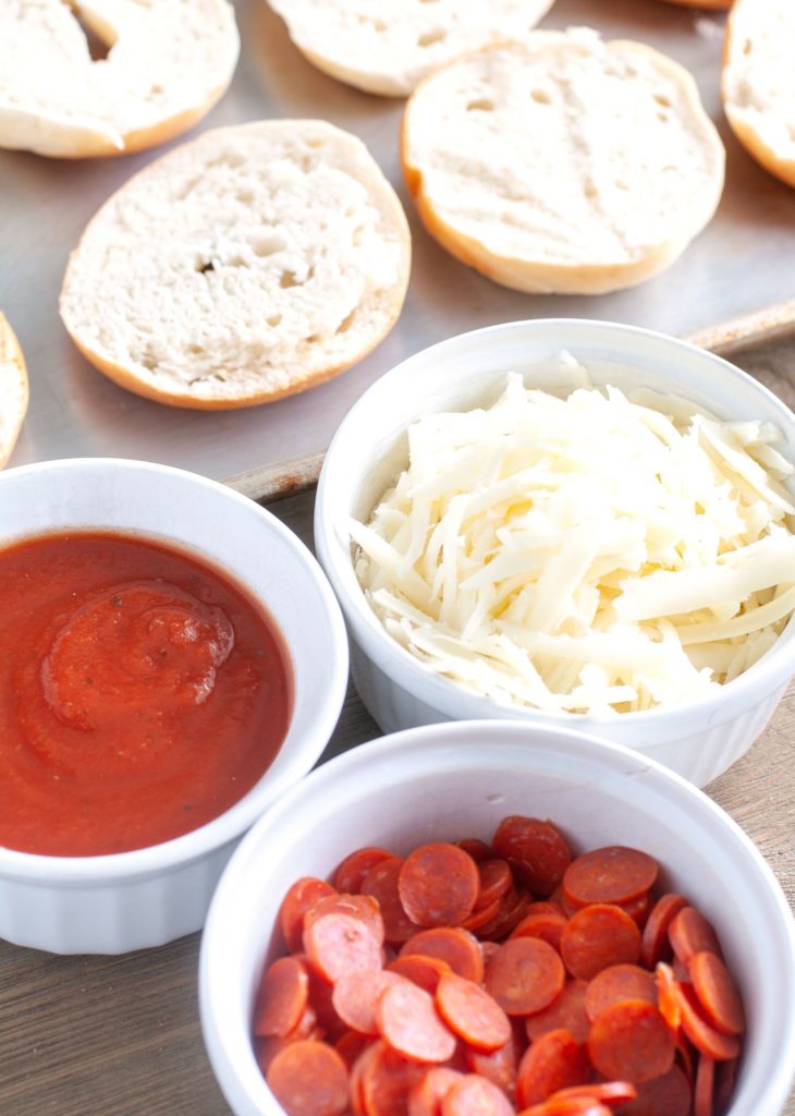 Mini bagels, bowl of sauce, bowl of shredded mozzarella cheese, bowl of mini pepperoni