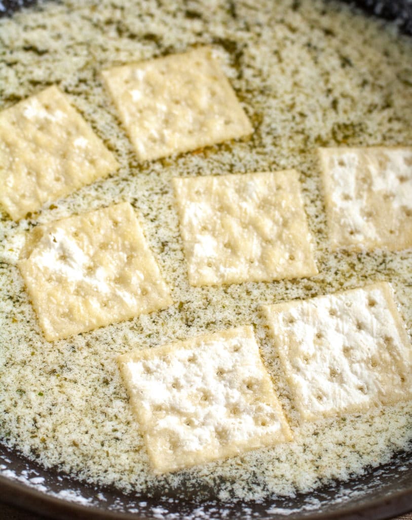 Crackers laying in melted butter and seasoning. 