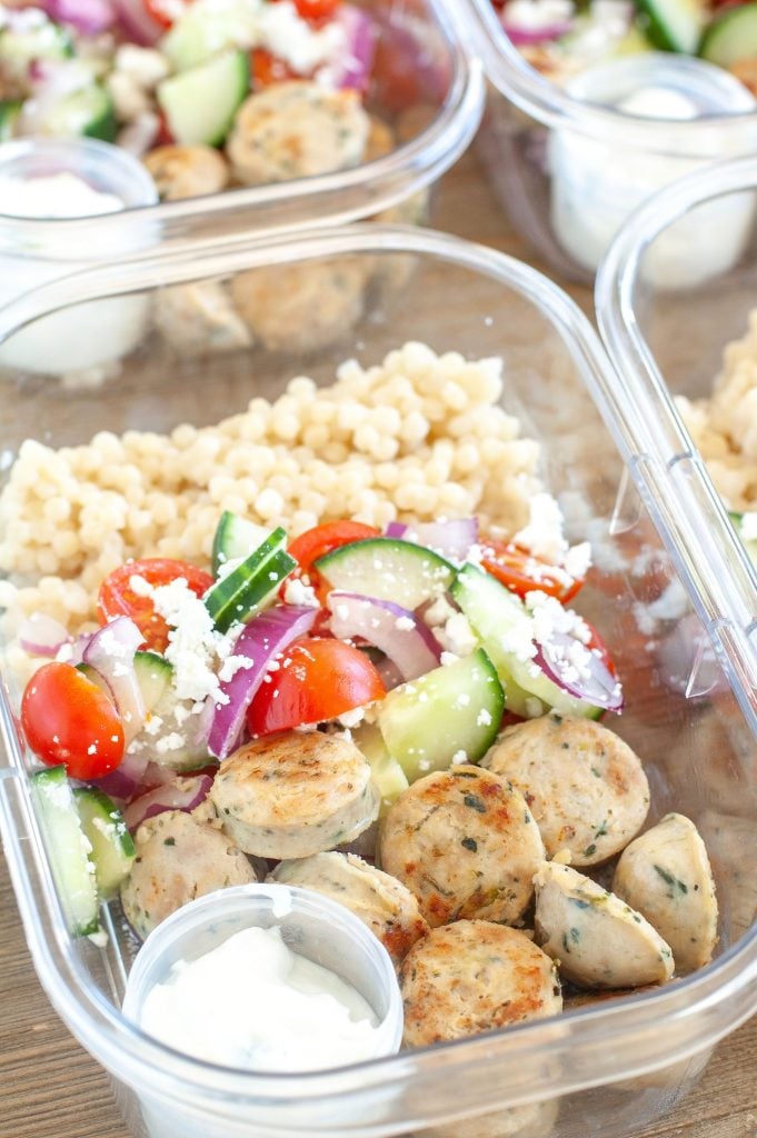 Meal prep container with chicken sausage, couscous and Greek Salad