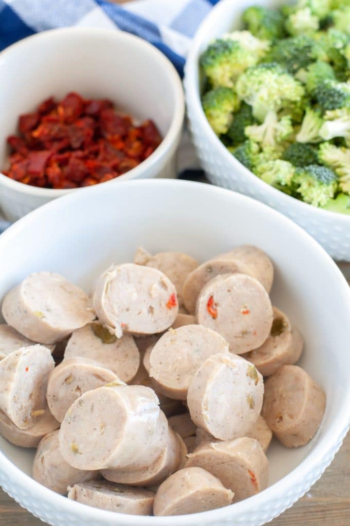 a bowl of chicken sausage. a bowl of sun dried tomatoes and a bowl of broccoli