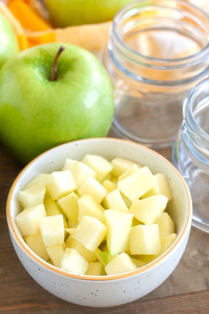 Apple Pie Filling Diced apples in a bowl with empty jars and an apple