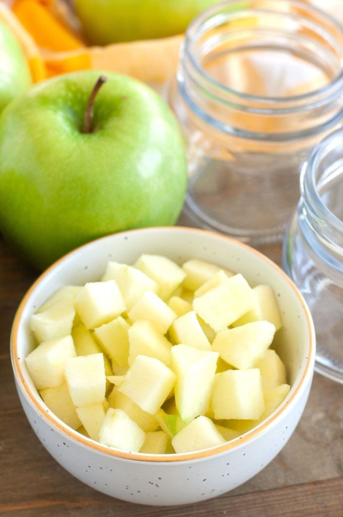 Diced apples in a bowl with empty jars and an apple