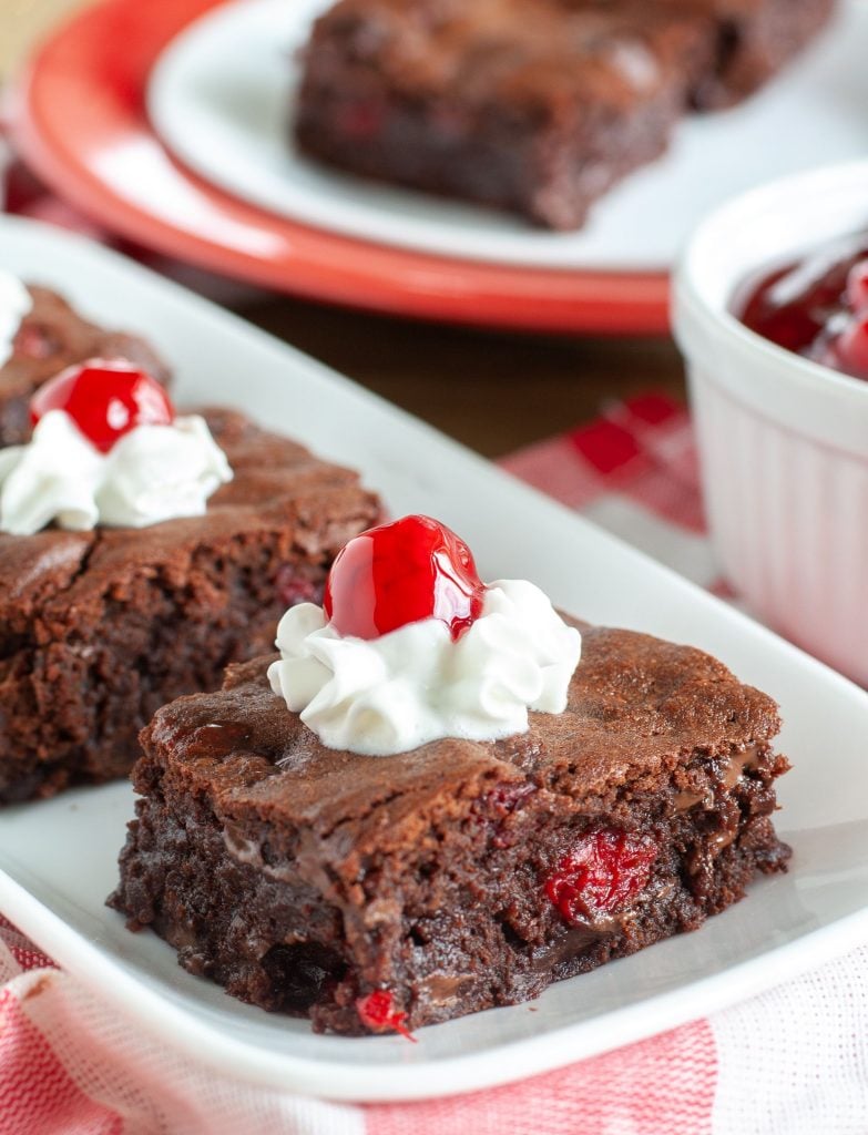 Plate of black forest brownies topped with whipped cream and cherries