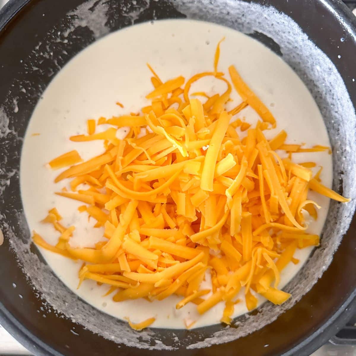 Saucepan with sauce and shredded cheese.