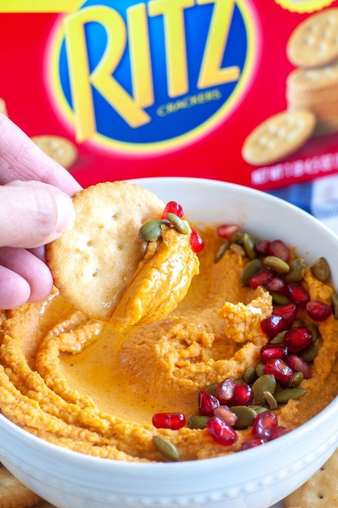 bowl of pumpkin hummus dip with a cracker dipping in