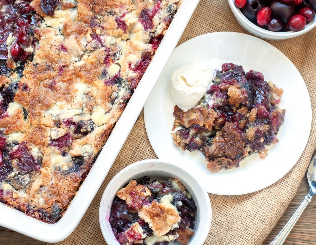 Baking dish with dump cake and a plate with dump cake and bowl of cranberries cherries