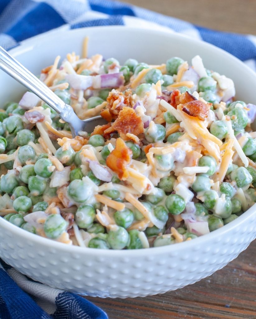 Pea salad topped with bacon in a white bowl with a spoon