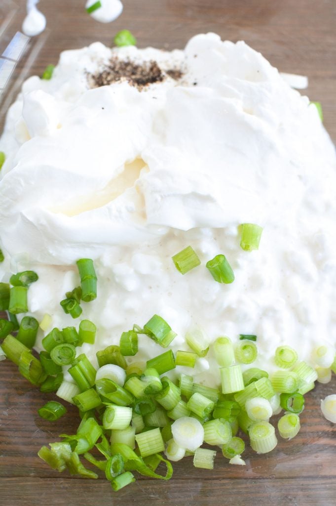 Glass bowl with sour cream, cottage cheese, green onion and black pepper