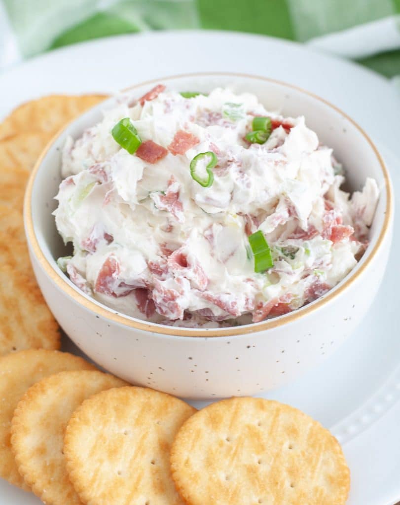 A white plate with a small bowl of chipped beef dip surrounded by crackers