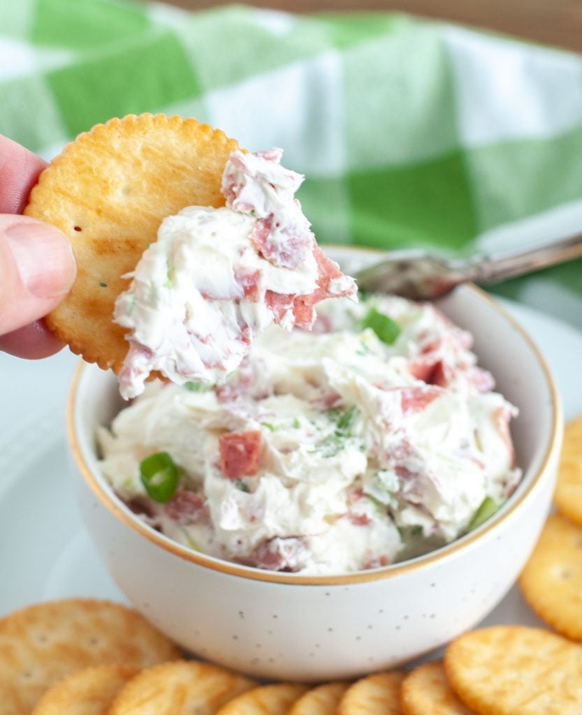 Chipped Beef Dip on a cracker being held above dip bowl
