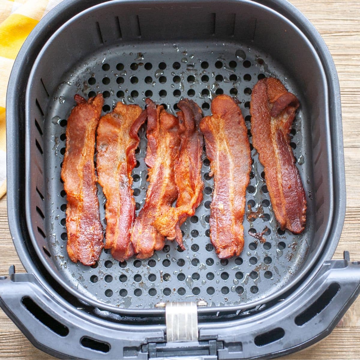 Cooked bacon in an air fryer basket.
