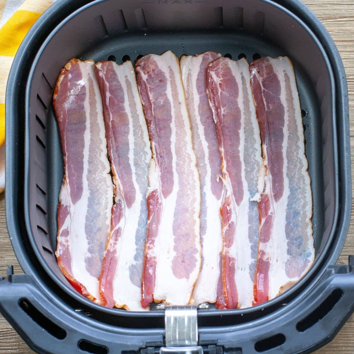 Uncooked bacon in an air fryer basket.