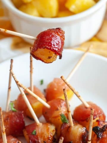 Bacon wrapped pineapple on a toothpick being held above a plate