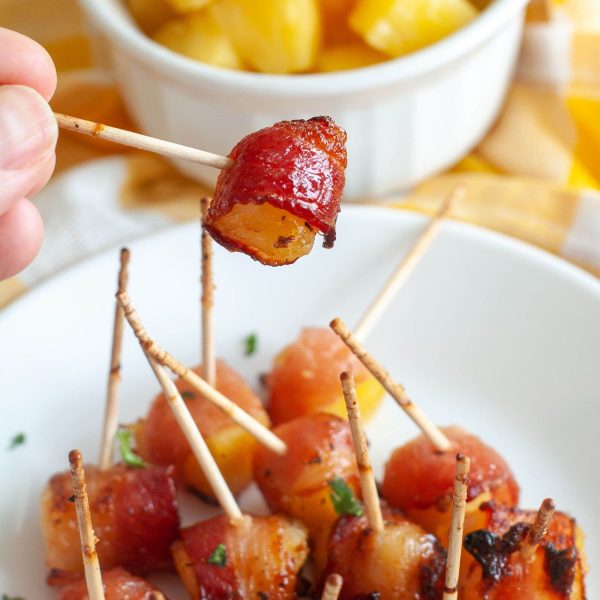 Bacon wrapped pineapple on a toothpick being held above a plate