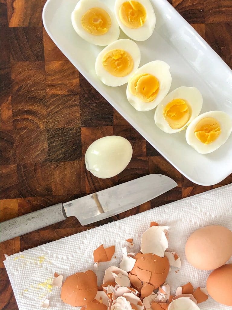 White plate with halved eggs on it, a knife and a paper towel with broken egg shells