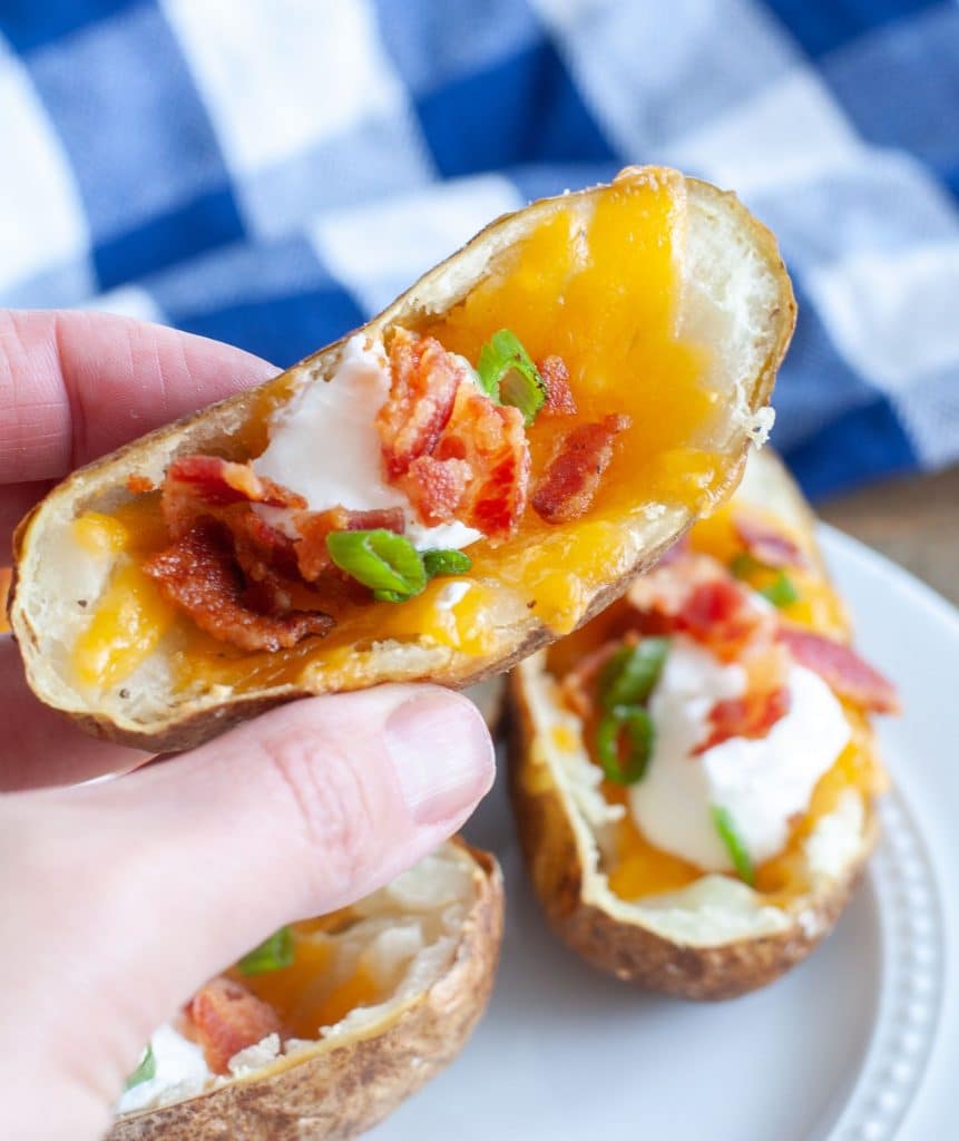 Hand holding an air fried potato skin with cheese, bacon and sour cream