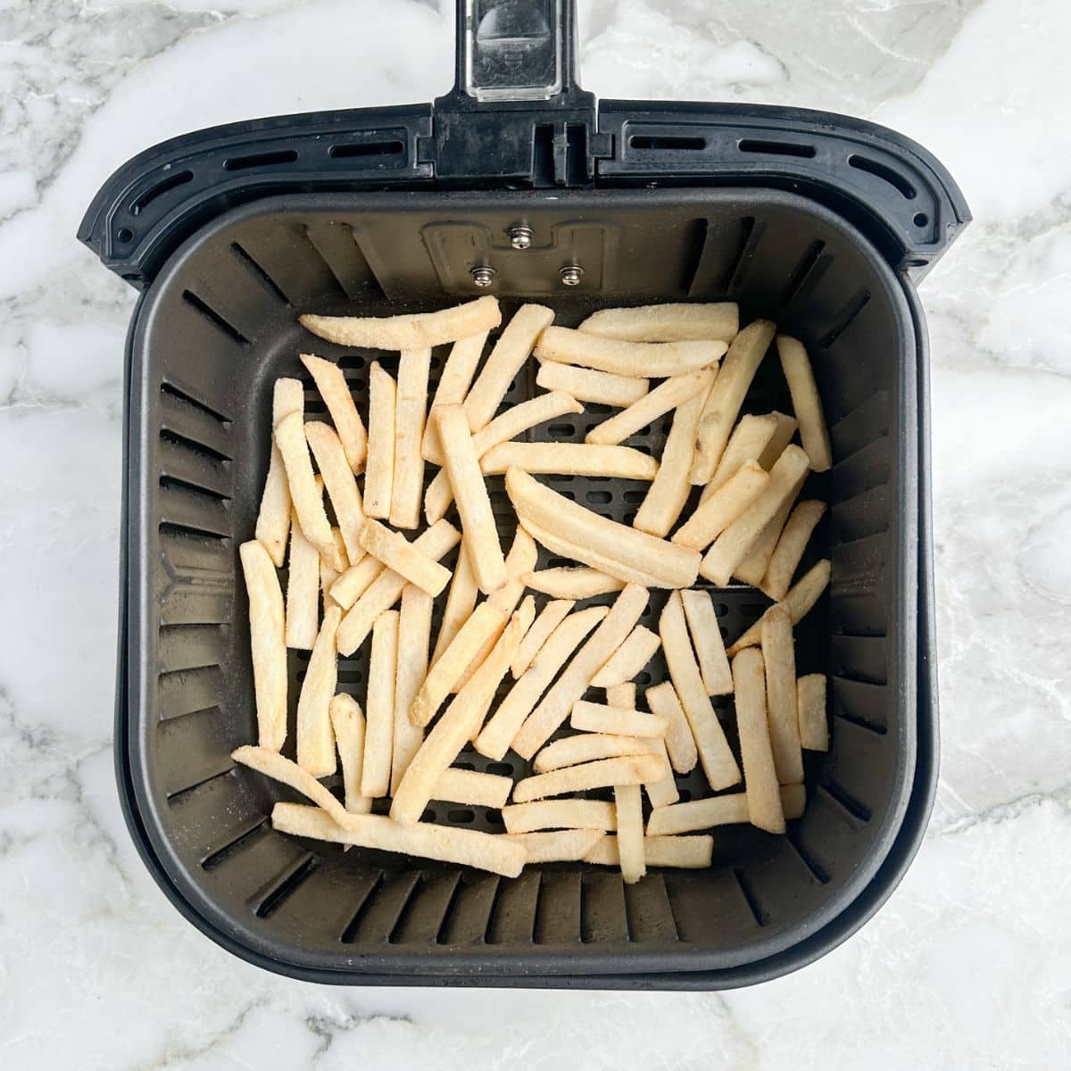 Air fryer basket with frozen french fries.