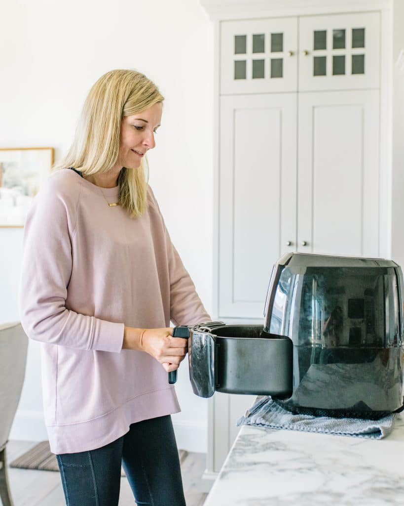 A woman standing by an air fryer. 