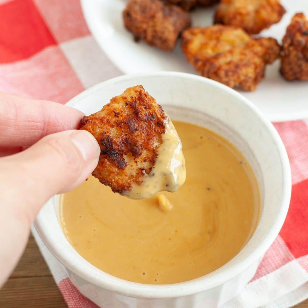 Hand holding chicken nugget dipped in sauce