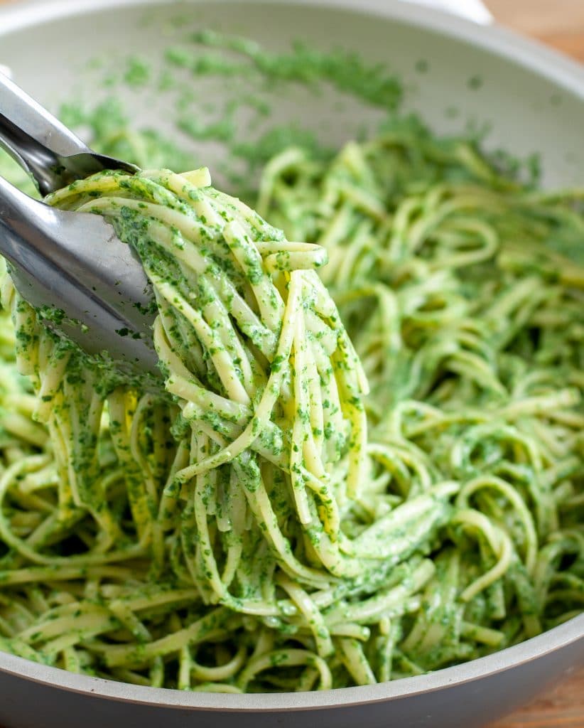 Green pasta in tongs