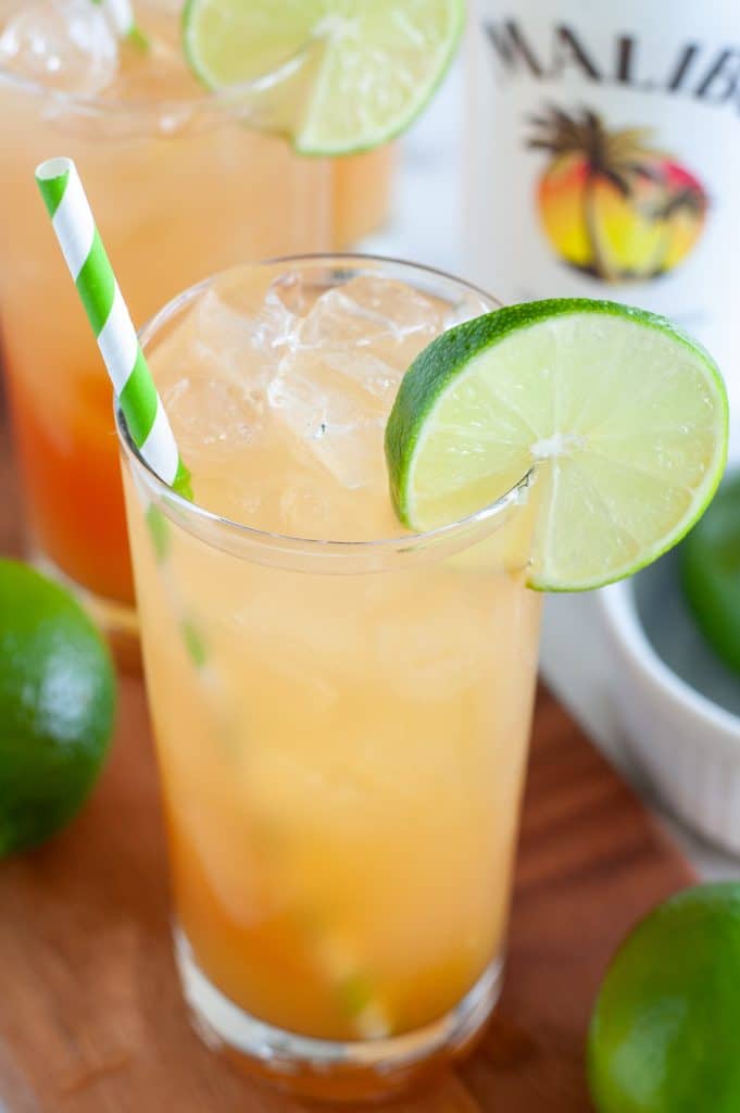 pineapple juice and cranberry juice in a glass with green striped straw and lime slice