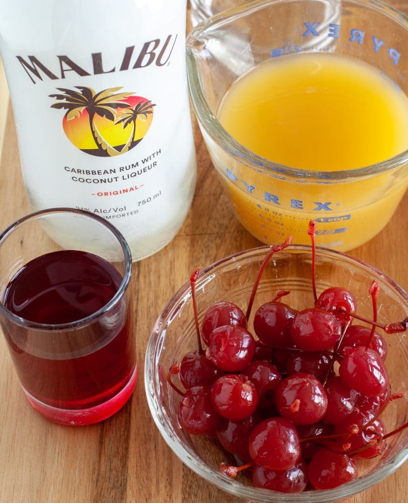 bottle of malibu rum, pineapple juice, bowl of cherries and cherry juice