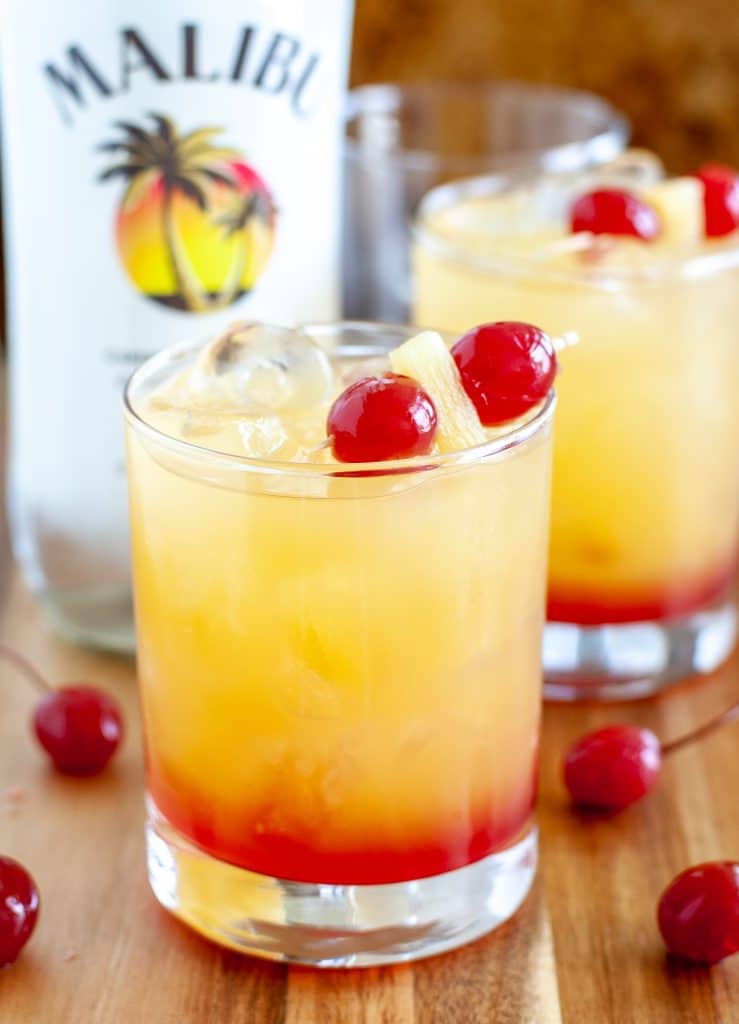 Rum cocktail in a glass with cherries and bottle in background