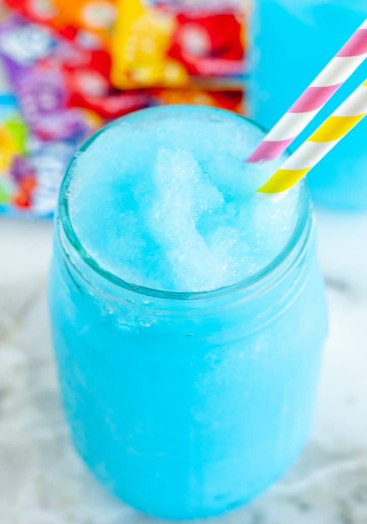 Blue slushie in a glass with kool-aid packets on the table