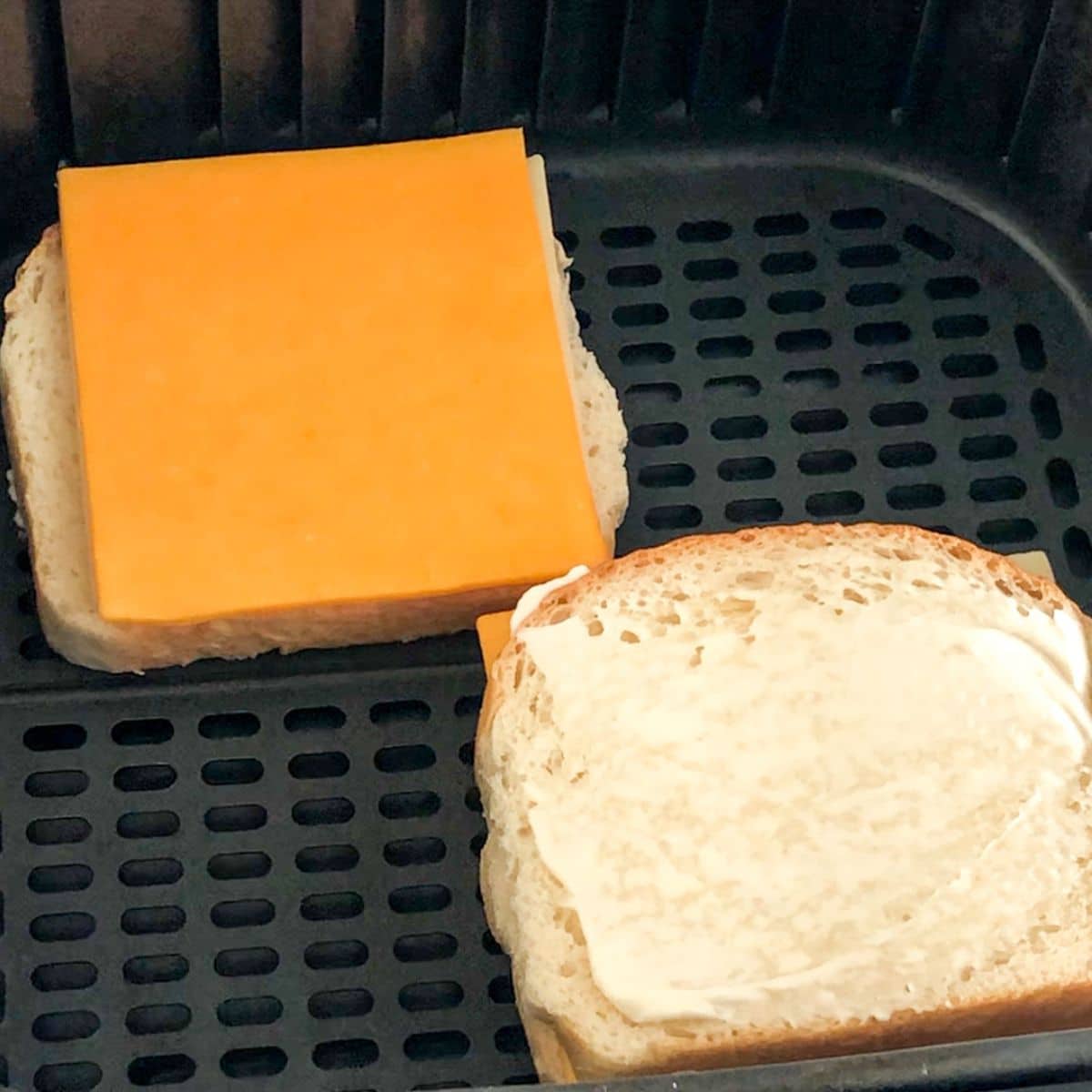 Bread topped with butter and sliced cheese in an air fryer.