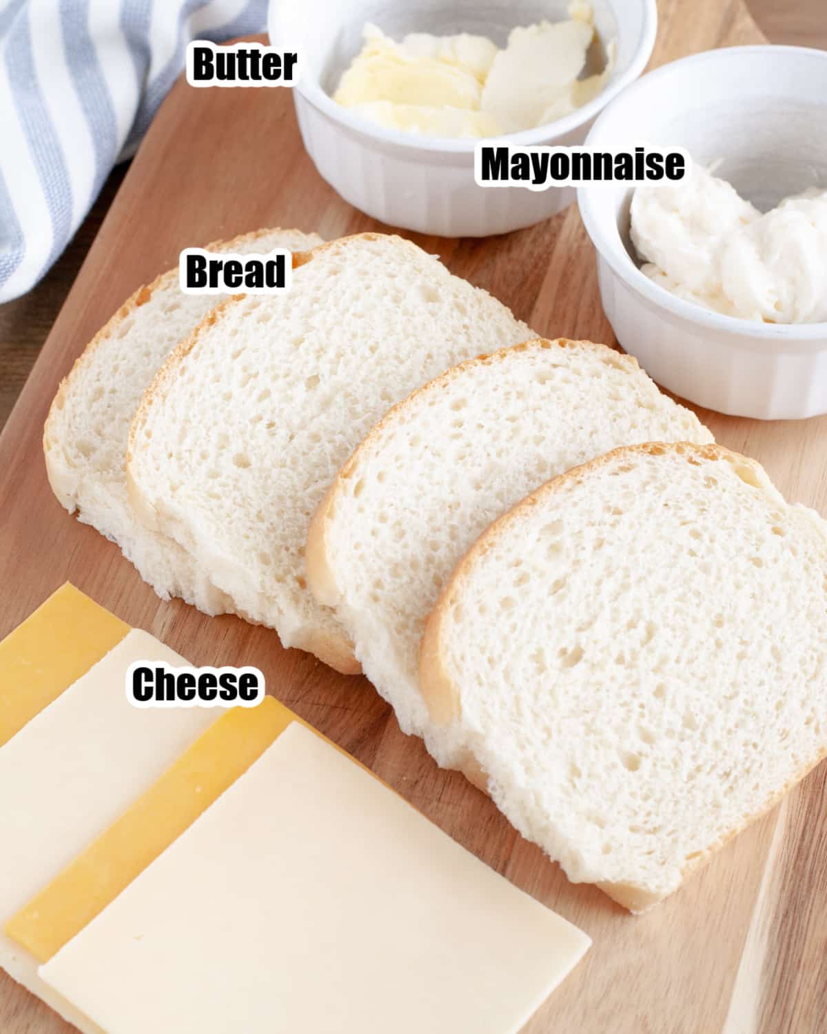 Slices of cheese, bread, and mayonnaise on a cutting board. 