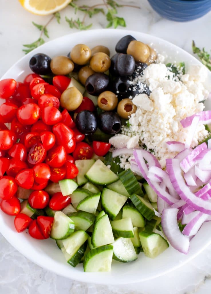 cucumbers, tomatoes, onion, olives and cheese in bowl