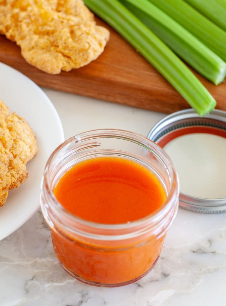buffalo sauce in a jar with chicken in the background