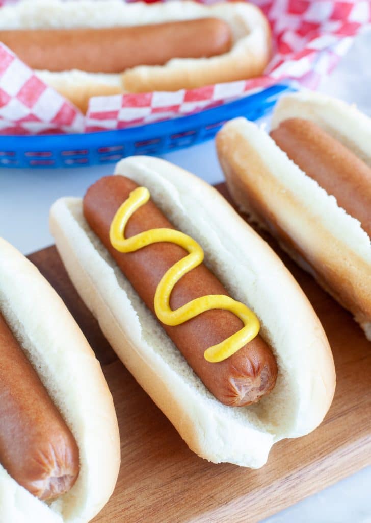 Three hotdogs in buns on a board 