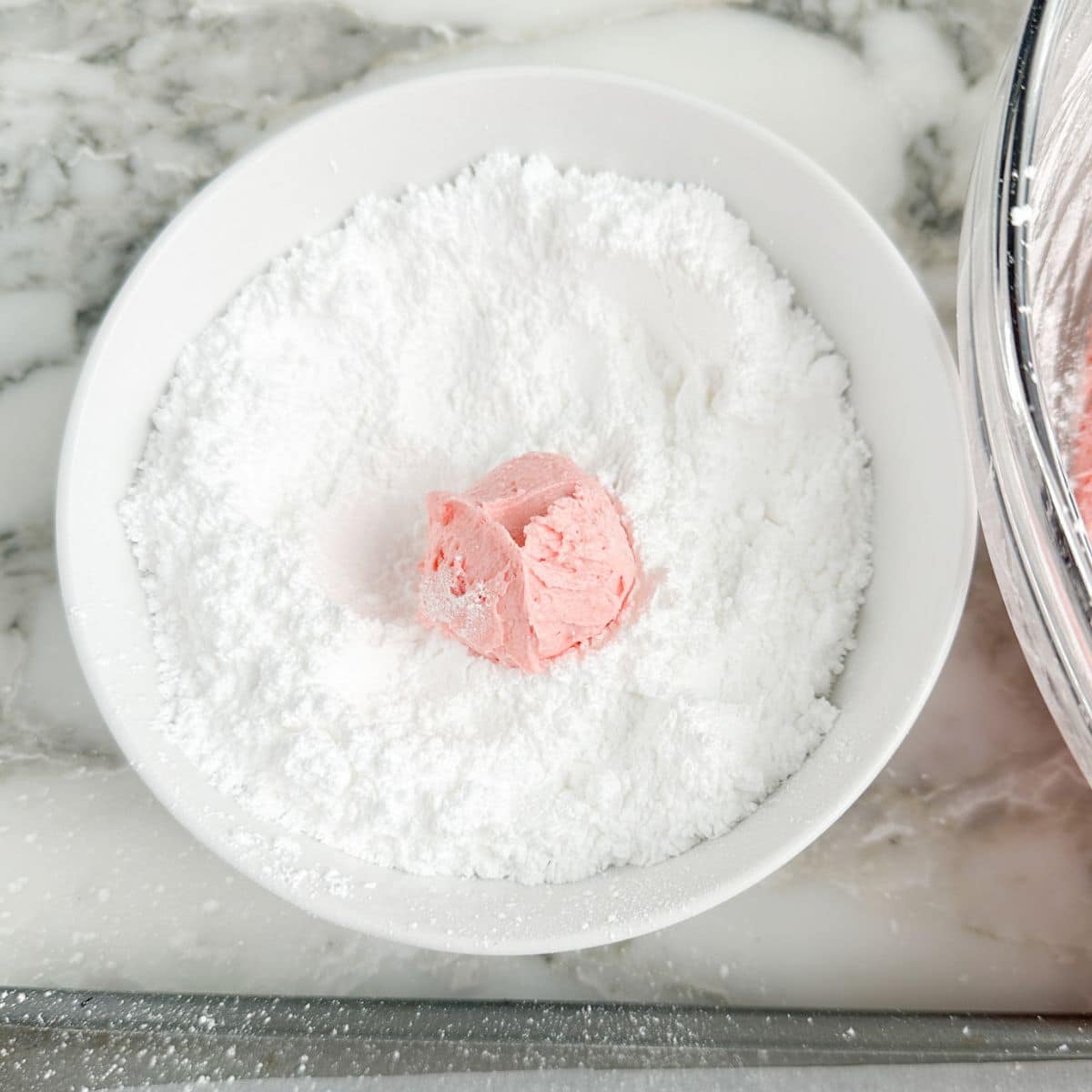Bowl of powdered sugar with strawberry cookie ball.