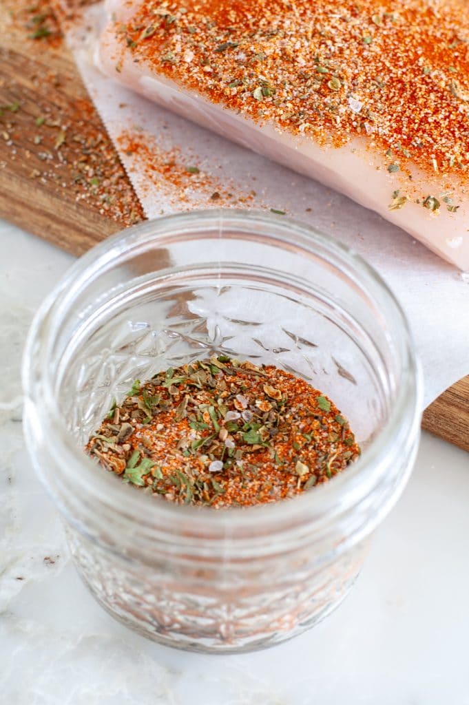 Spices in a jar with a piece of chicken and seasonings