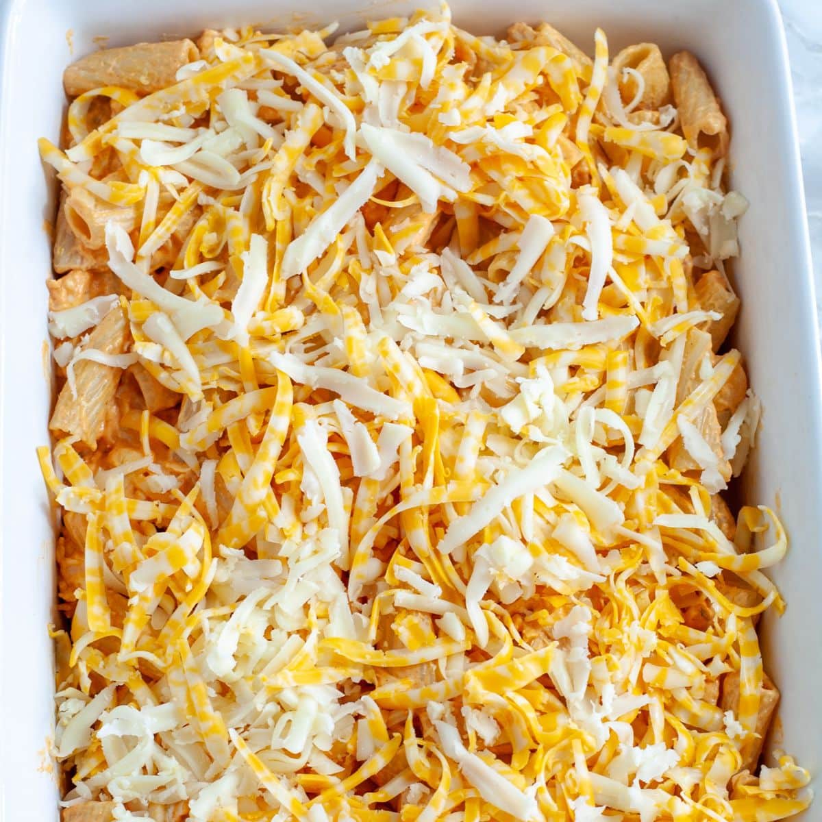 Baking dish with buffalo chicken pasta topped with shredded cheese.