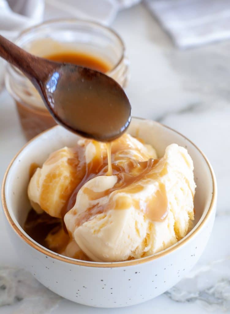 Spoon drizzling dessert topping over ice cream. 