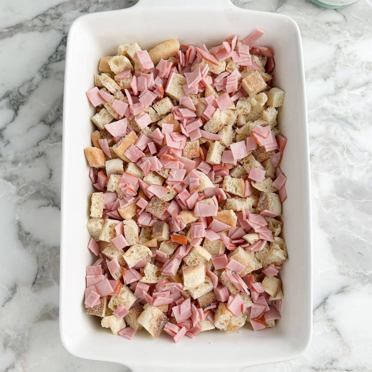 Casserole dish with diced English muffins and diced Canadian bacon.