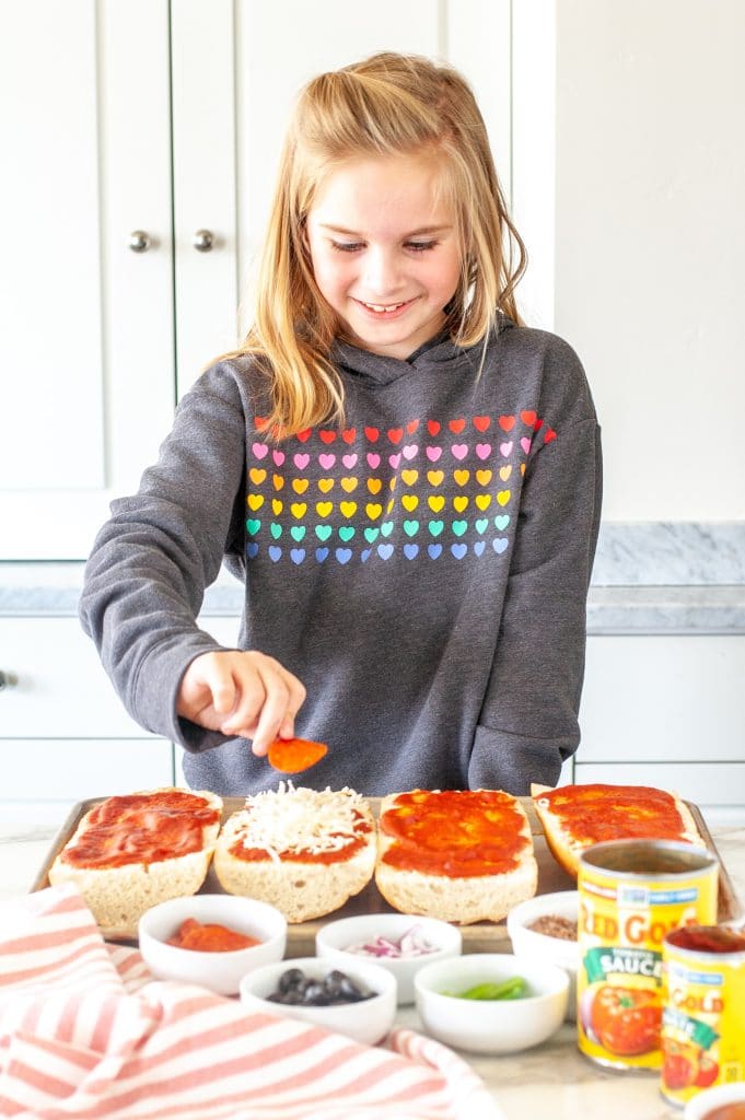 Girl making french bread pizza.