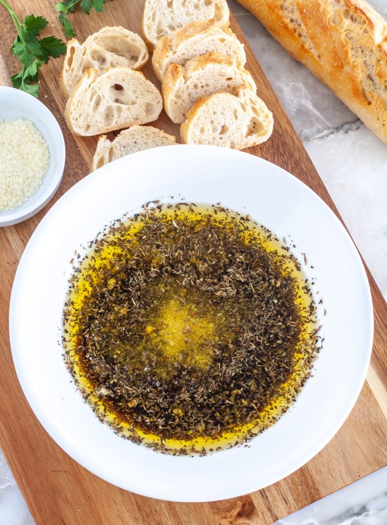 Oil and herbs in bowl with sliced bread.