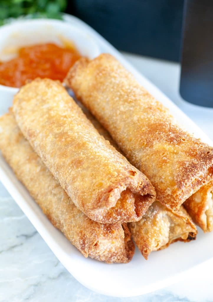 Plate with stacked egg rolls and bowl of sauce.