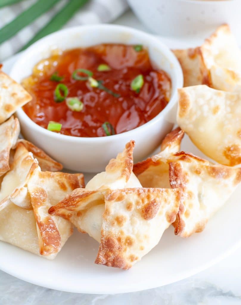 Cream cheese wontons on plate with bowl of sauce. 