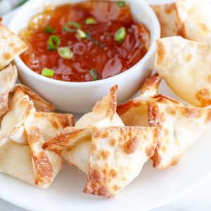 Wontons on plate with bowl of sauce.