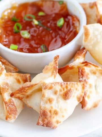 Wontons on plate with bowl of sauce.