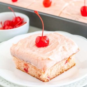 Piece of cake on plate with cherry frosting and cherry on top.