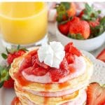 Stack of pancakes with strawberries and whipped cream.